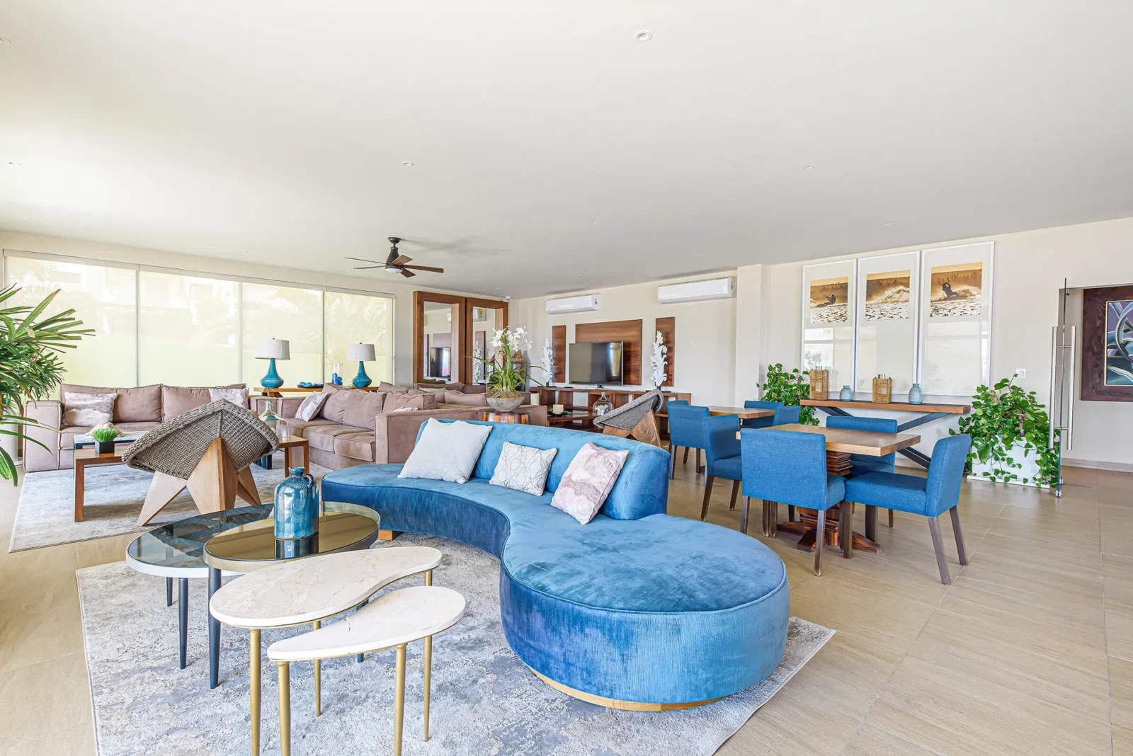 Spacious and modern resort living room with elegant decor, blue velvet seating, and large windows offering natural light and views of lush surroundings.
