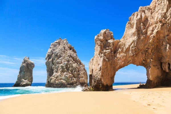 Iconic rock formations and golden sands at Land's End in Cabo San Lucas under a bright blue sky.