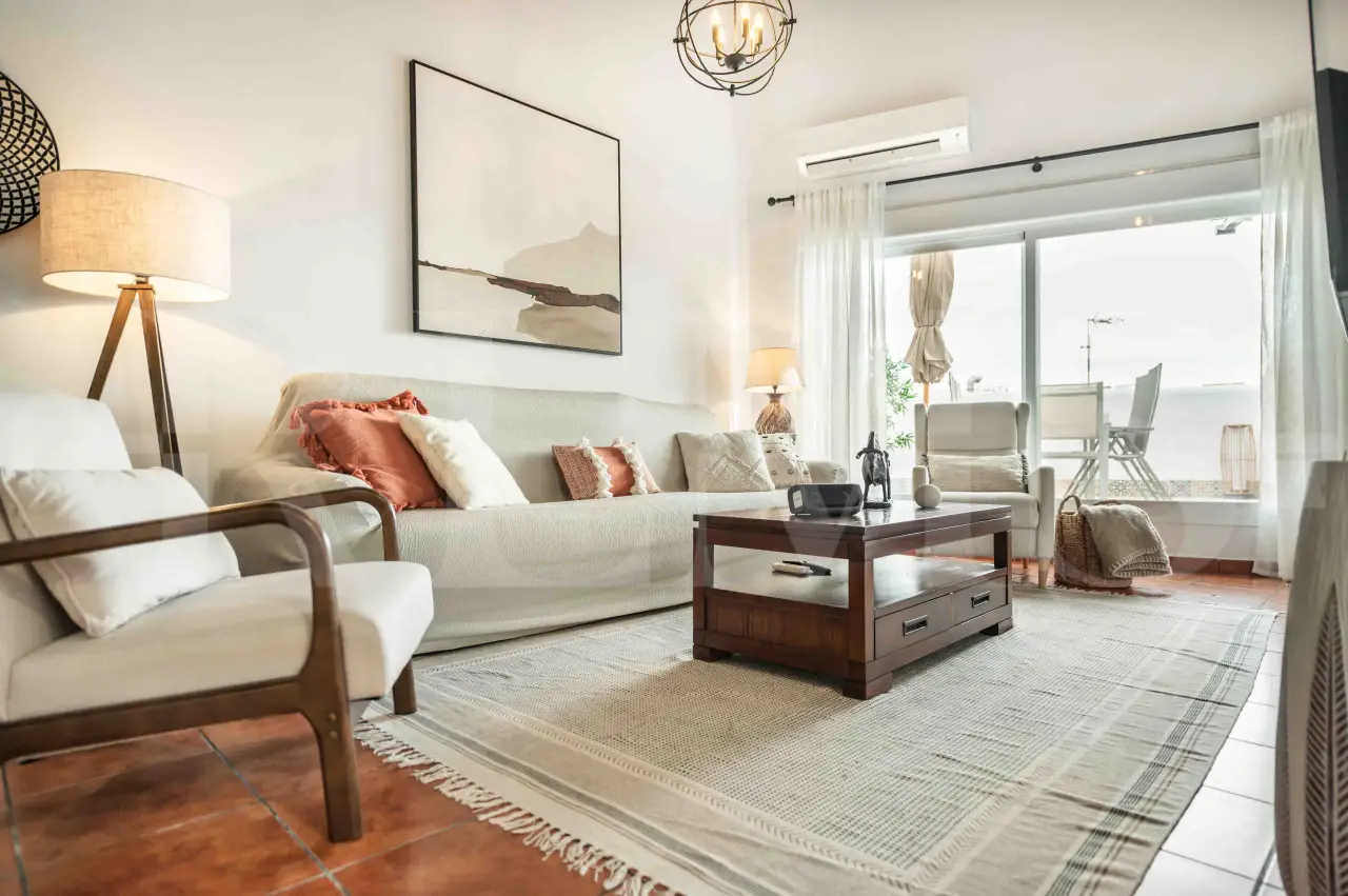 Stylish Andalusian-inspired living room with natural light, terracotta floors, and cozy neutral-toned furnishings in a luxury apartment for 4 guests in Malaga, Spain.