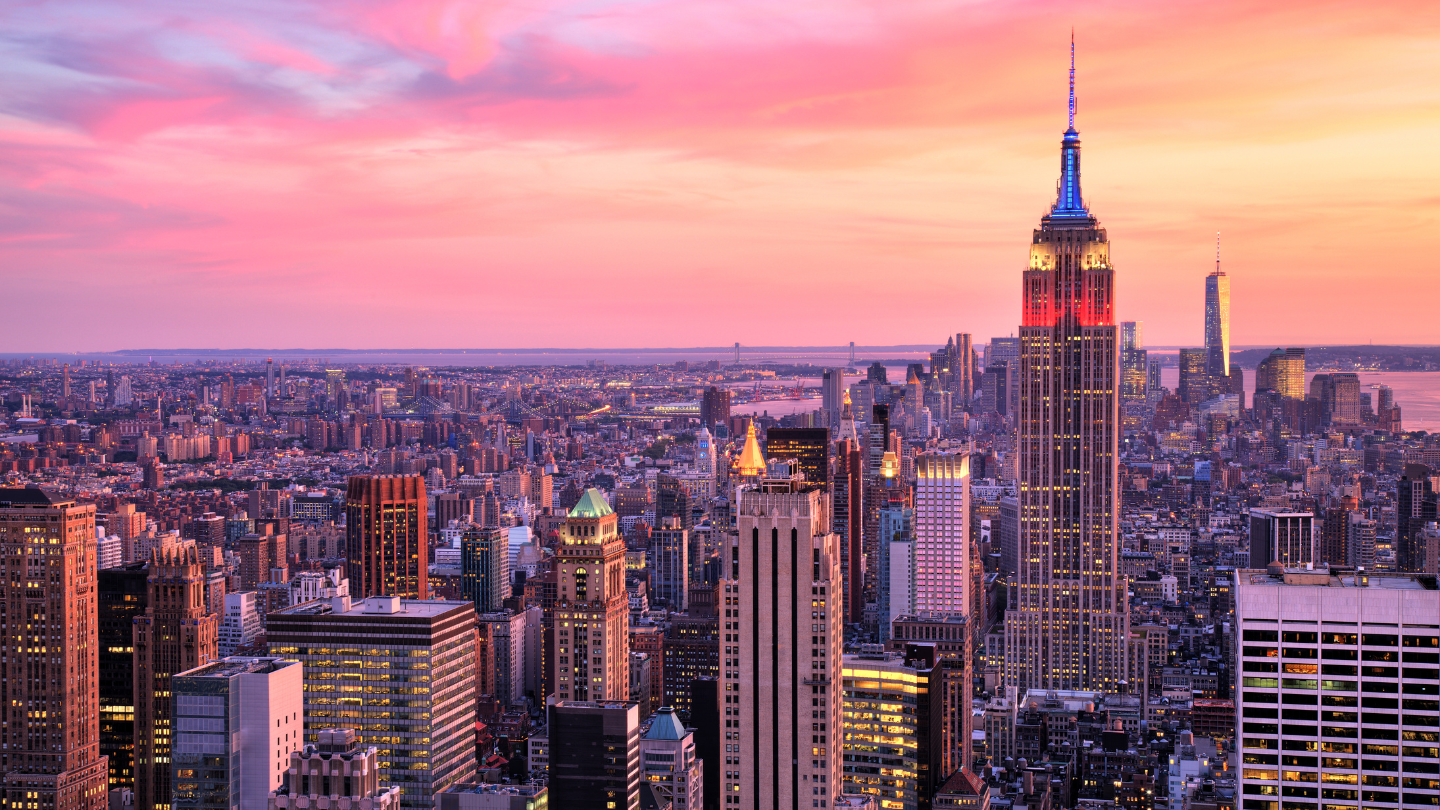 New York City Skyline at Sunset – A breathtaking aerial view of New York City at sunset, featuring the Empire State Building illuminated against a vibrant pink and orange sky. A perfect auction package destination for an unforgettable urban getaway.