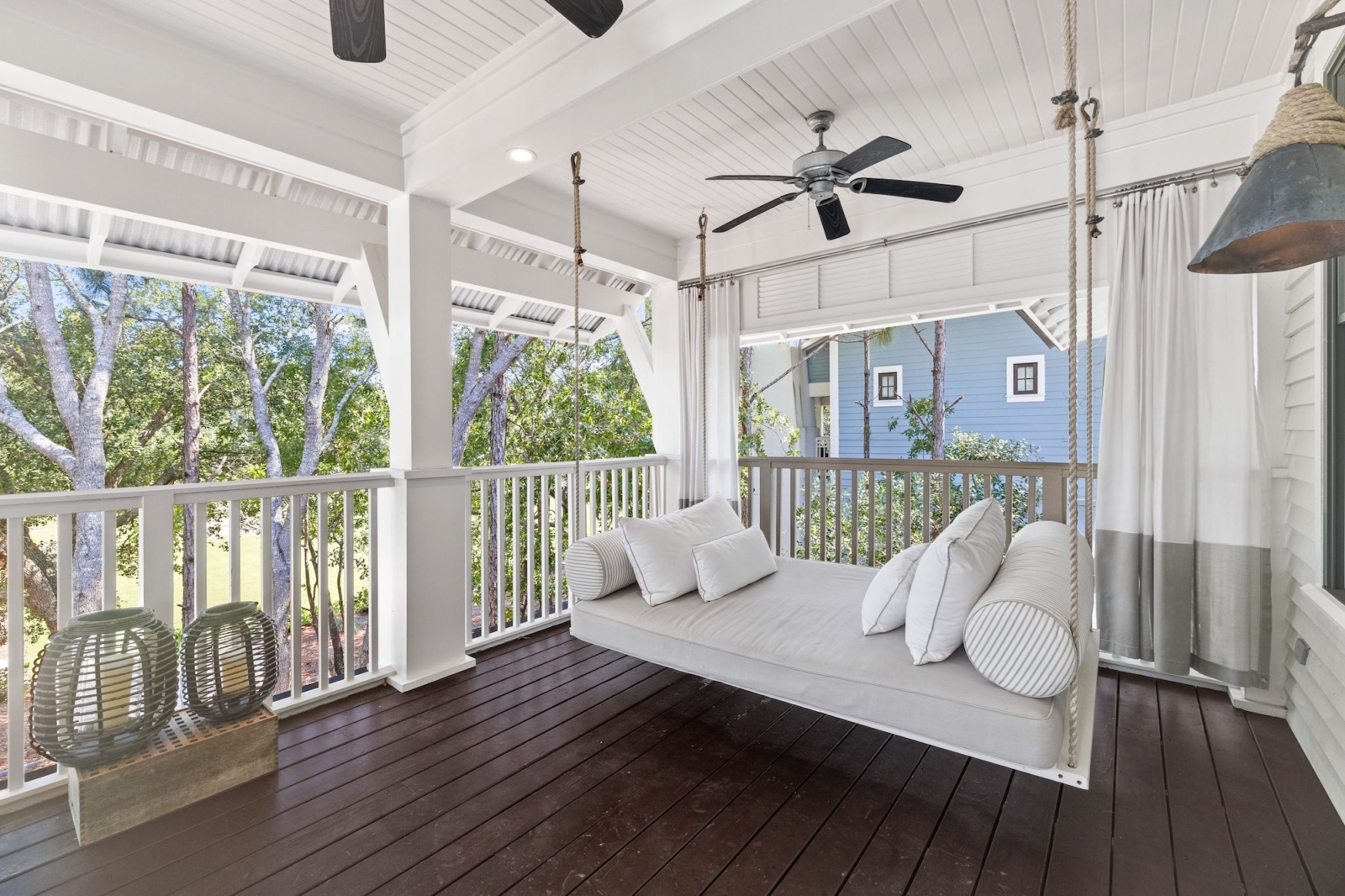 Covered balcony with swinging daybed and ceiling fans, overlooking lush trees in a luxury Watercolor, Florida vacation home