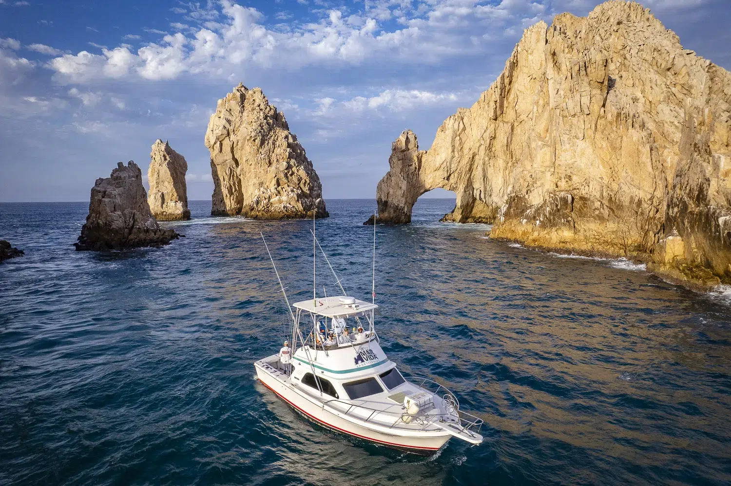 Fishing charter boat cruising near the iconic rock formations of Land’s End in Cabo San Lucas, Mexico, with clear skies and shimmering water.